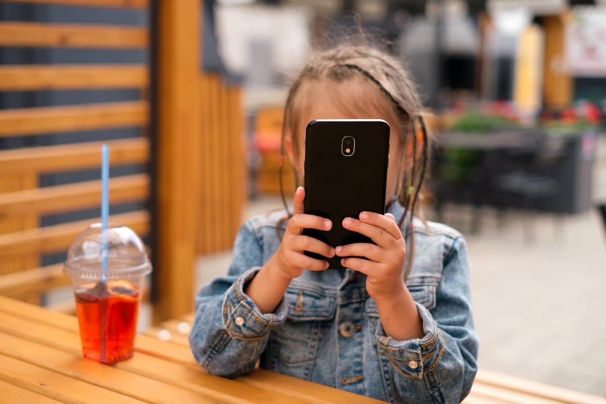 a-child-is-playing-with-a-phone-while-sitting-at-a-2022-03-05-22-19-07-utc